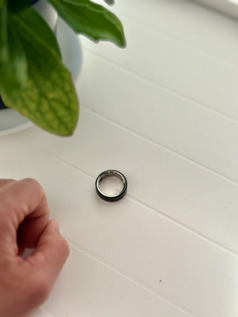 An Oura Ring resting on a white table next to a plant.